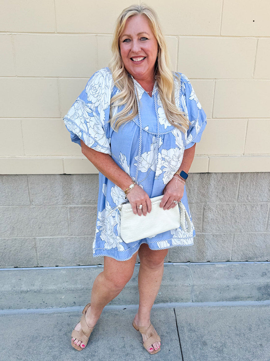 Floral babydoll mini dress with puff sleeves, ruffle collar, and striped trim displayed in a boutique setting.