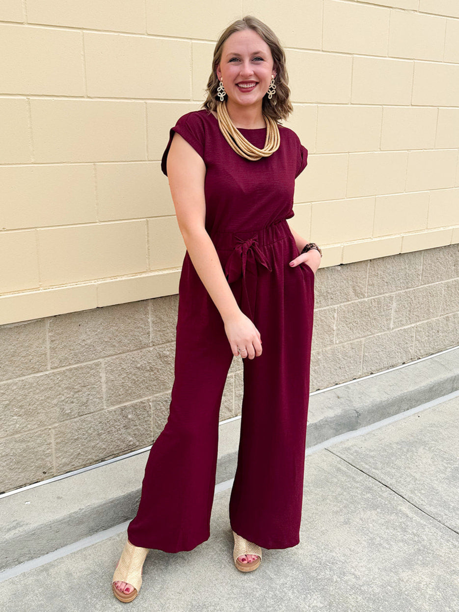 Garnet short-sleeve jumpsuit with elastic waist, front tie, high scoop neckline, and side pockets. Sporty, flattering, and perfect for Gameday style.