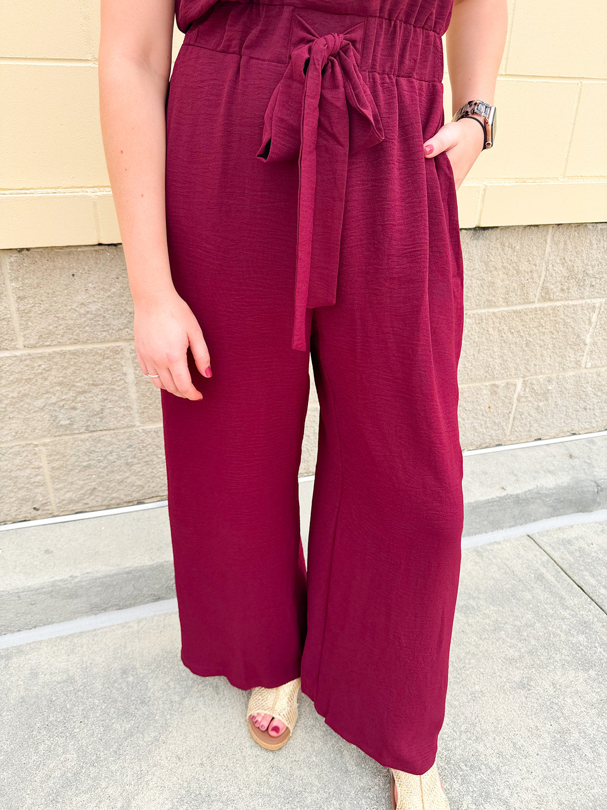 Garnet short-sleeve jumpsuit with elastic waist, front tie, high scoop neckline, and side pockets. Sporty, flattering, and perfect for Gameday style.