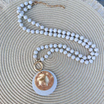 Cream beaded necklace with gold accents and a layered hammered gold and cream pendant, styled for versatile wear.
