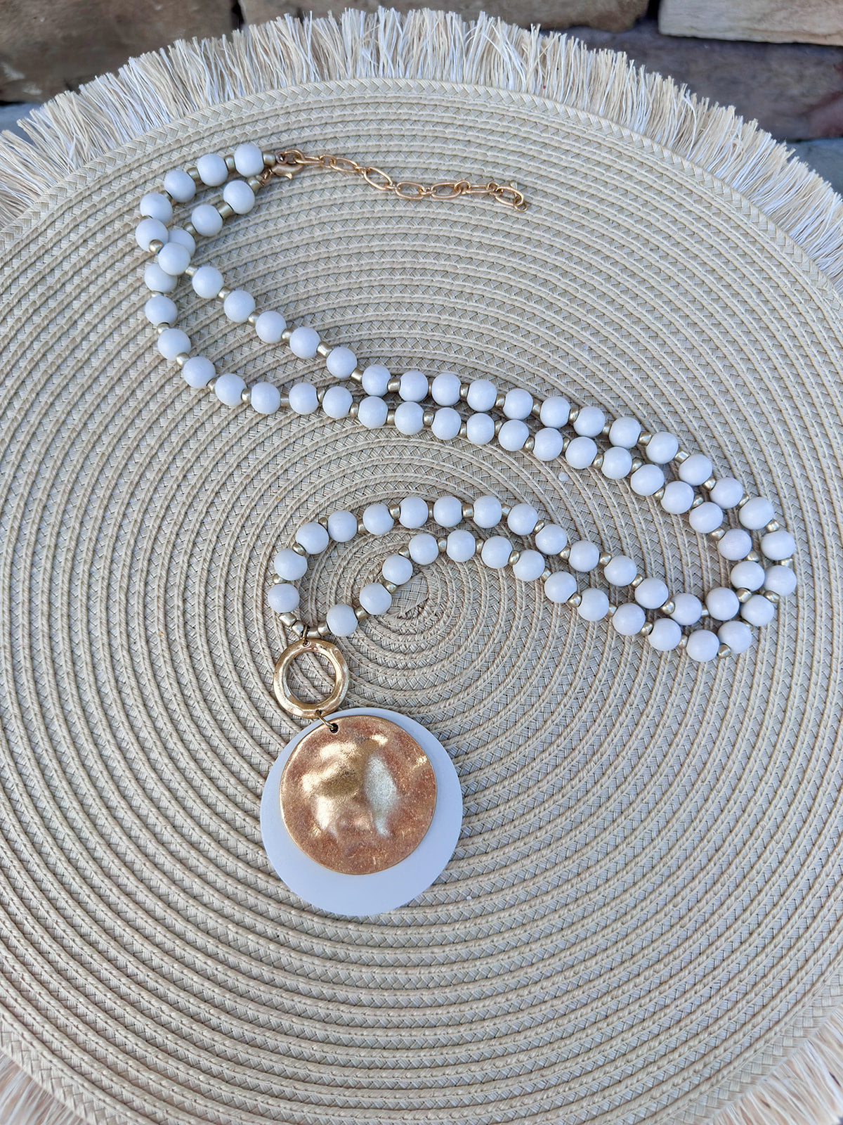 Cream beaded necklace with gold accents and a layered hammered gold and cream pendant, styled for versatile wear.