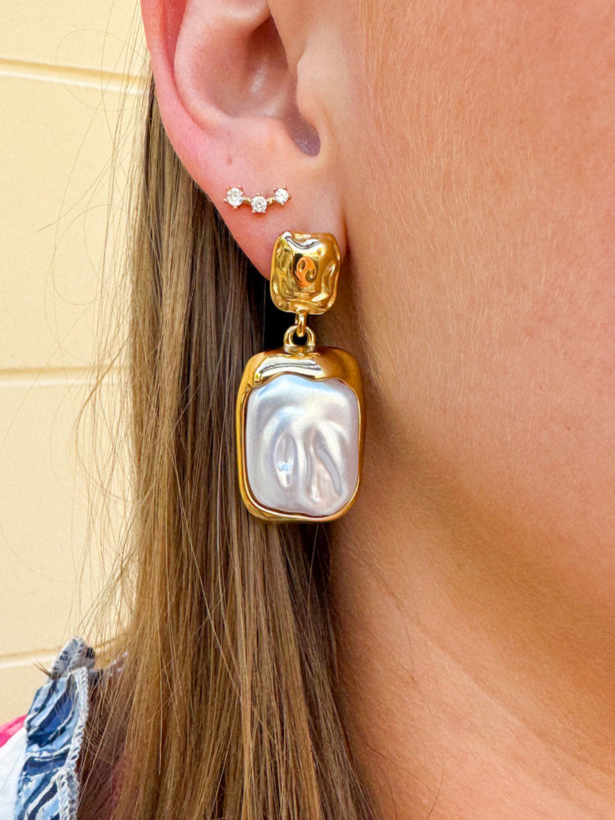 Gold cluster stud earrings featuring a large rectangular pearl hanging from a delicate gold cluster, styled as an elegant statement accessory.