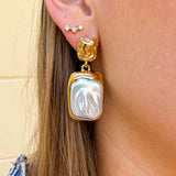 Gold cluster stud earrings featuring a large rectangular pearl hanging from a delicate gold cluster, styled as an elegant statement accessory.