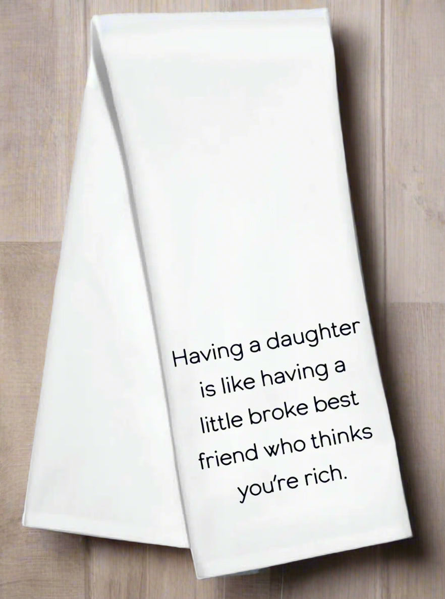 White kitchen towel with the phrase “Having a daughter is like having a little broke best friend who thinks you’re rich”