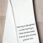White kitchen towel with the phrase “Having a daughter is like having a little broke best friend who thinks you’re rich”