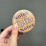 Round button with garnet “Noles, Noles, Noles” lettering on a subtle gold animal print background, styled as a gameday bag accessory.