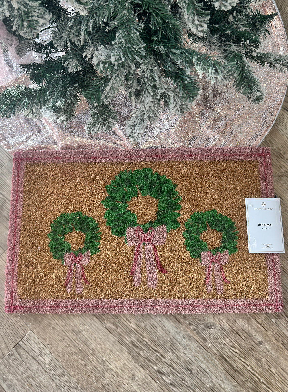 Christmas doormat with green wreaths, pink bows, and pink border.