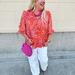 Pink and orange paisley print blouse with frilled tie neckline and three-quarter peasant sleeves against a neutral background