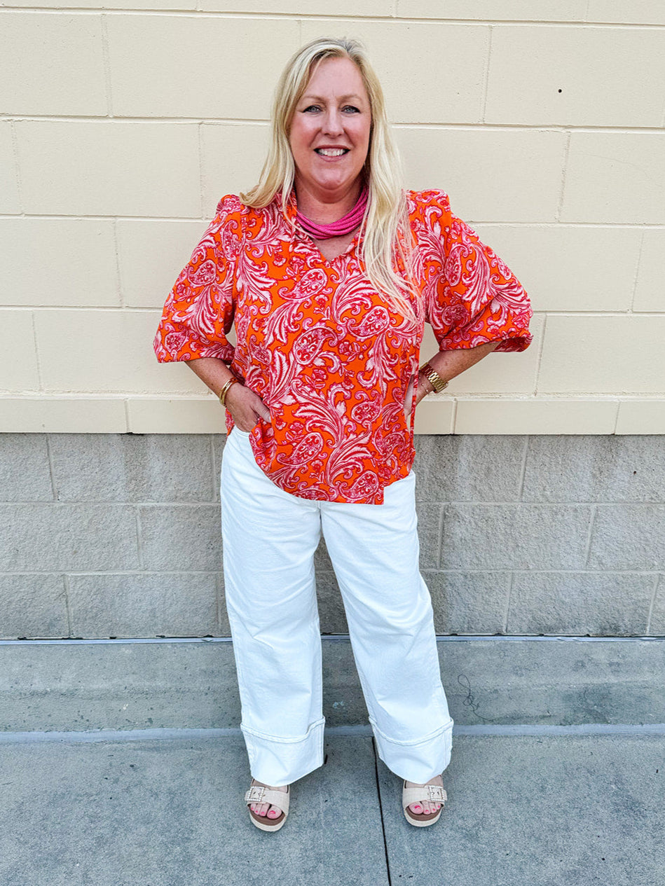 Pink and orange paisley print blouse with frilled tie neckline and three-quarter peasant sleeves against a neutral background