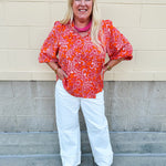 Pink and orange paisley print blouse with frilled tie neckline and three-quarter peasant sleeves against a neutral background