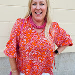 Pink and orange paisley print blouse with frilled tie neckline and three-quarter peasant sleeves against a neutral background