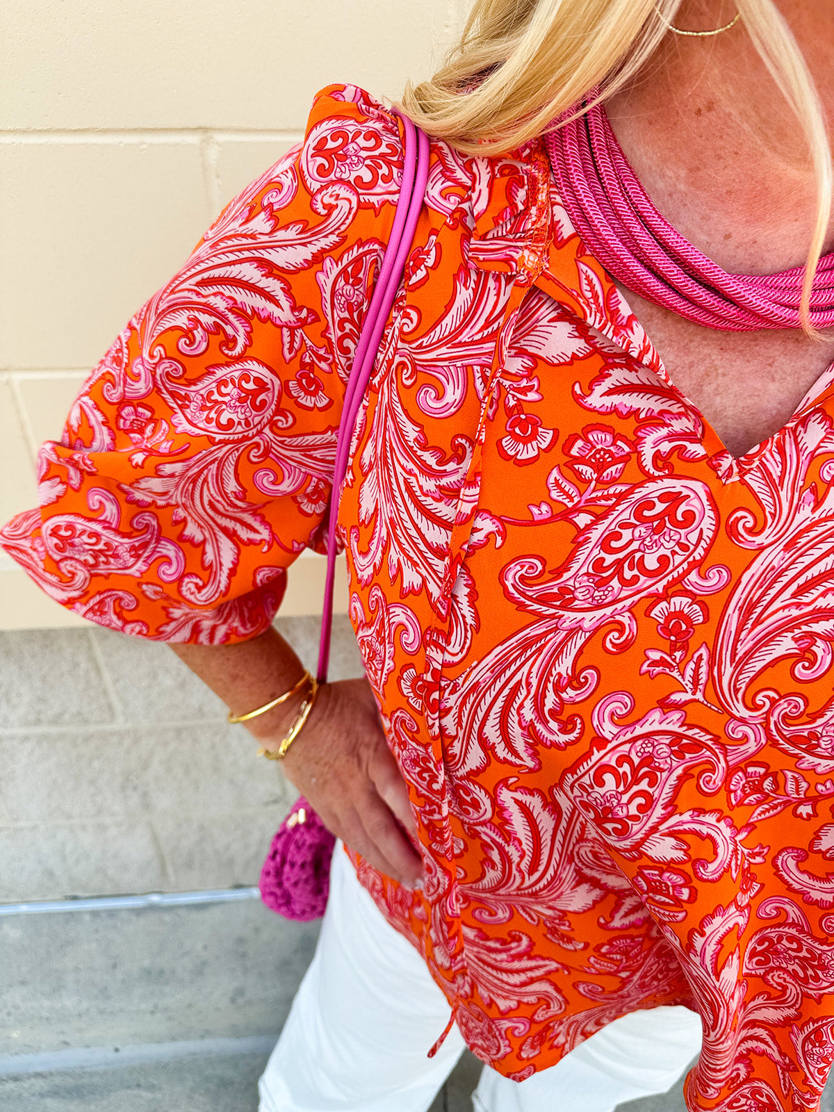 Pink and orange paisley print blouse with frilled tie neckline and three-quarter peasant sleeves against a neutral background