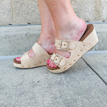 Raffia wedge sandal with slide-on design, dual straps, rhinestone buckles, and gold hardware embellishments