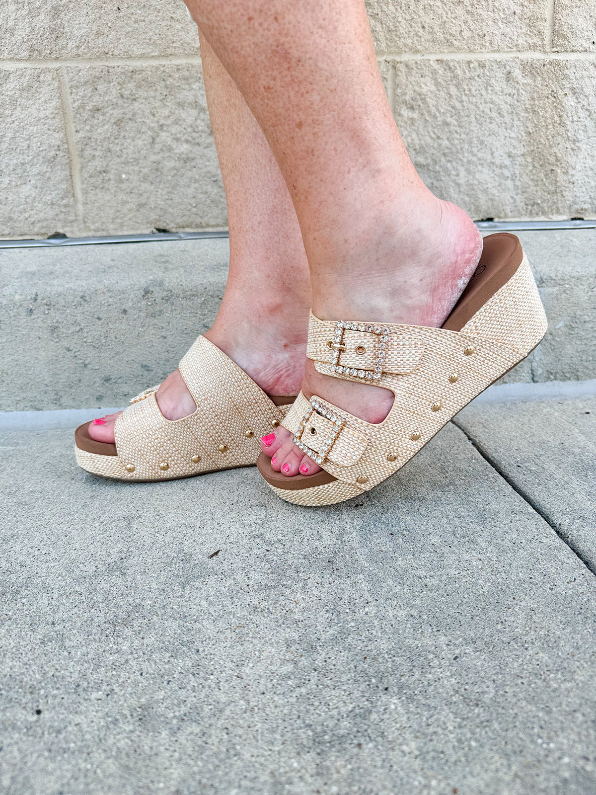 Raffia wedge sandal with slide-on design, dual straps, rhinestone buckles, and gold hardware embellishments