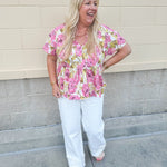 Pink floral babydoll top with ruffle collar, short sleeves, and a tie-neck detail, styled for a soft and feminine look.