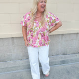 Pink floral babydoll top with ruffle collar, short sleeves, and a tie-neck detail, styled for a soft and feminine look.