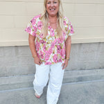 Pink floral babydoll top with ruffle collar, short sleeves, and a tie-neck detail, styled for a soft and feminine look.