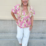 Pink floral babydoll top with ruffle collar, short sleeves, and a tie-neck detail, styled for a soft and feminine look.