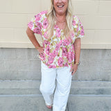 Pink floral babydoll top with ruffle collar, short sleeves, and a tie-neck detail, styled for a soft and feminine look.