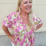 Pink floral babydoll top with ruffle collar, short sleeves, and a tie-neck detail, styled for a soft and feminine look.