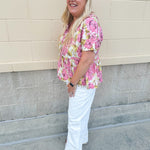 Pink floral babydoll top with ruffle collar, short sleeves, and a tie-neck detail, styled for a soft and feminine look.