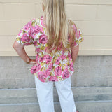 Pink floral babydoll top with ruffle collar, short sleeves, and a tie-neck detail, styled for a soft and feminine look.