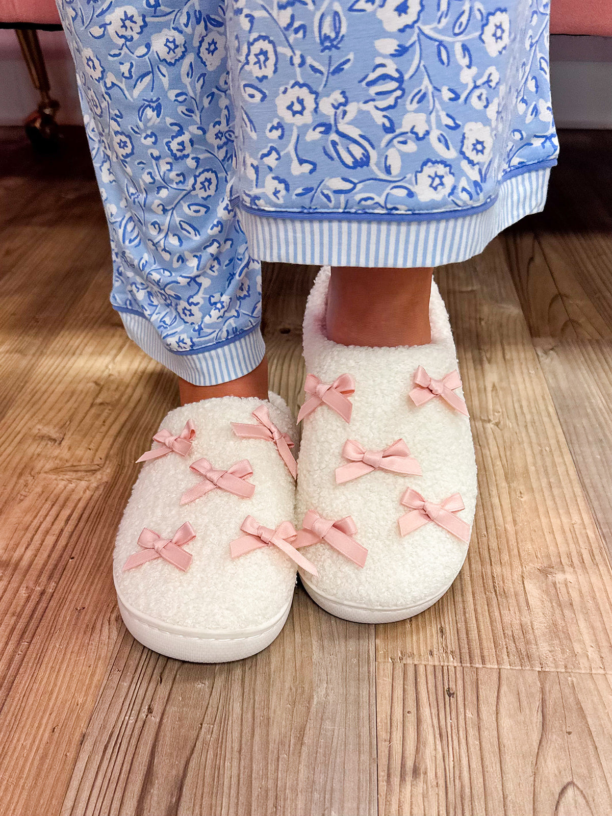 White sherpa closed-toe slippers decorated with small pink bows and pink insoles.