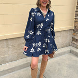 Navy mini dress with cream floral embroidery, long sleeves, and waist tie styled with boots.