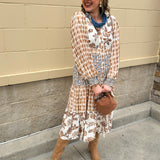 Tiered shirt dress in brown, cream, and blue mixed print with collared neckline, smocked details, and long sleeves.