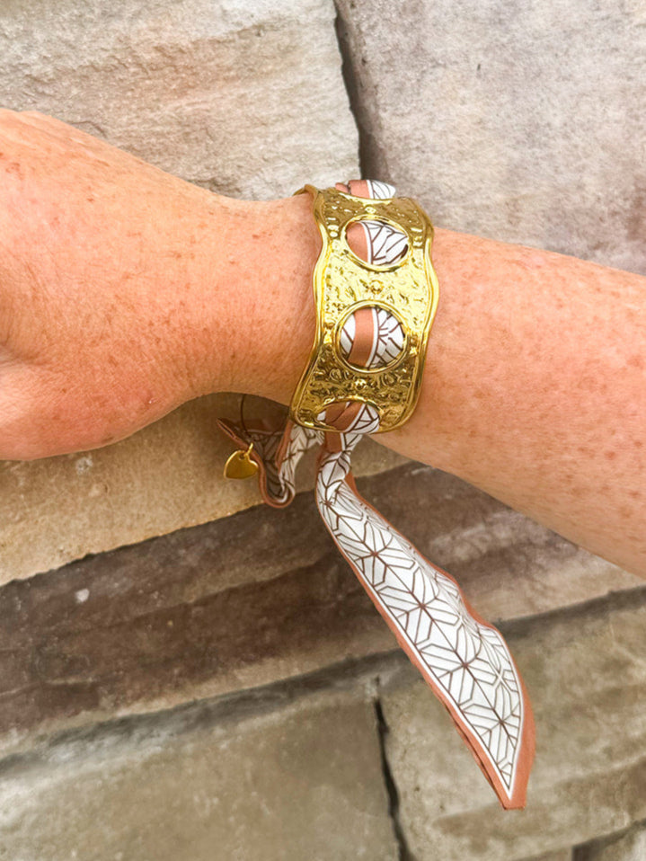 Gold cuff bracelet woven with geometric black-and-white scarf featuring a brown border; ties together for a bold yet feminine accessory.