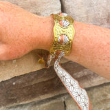 Gold cuff bracelet woven with geometric black-and-white scarf featuring a brown border; ties together for a bold yet feminine accessory.