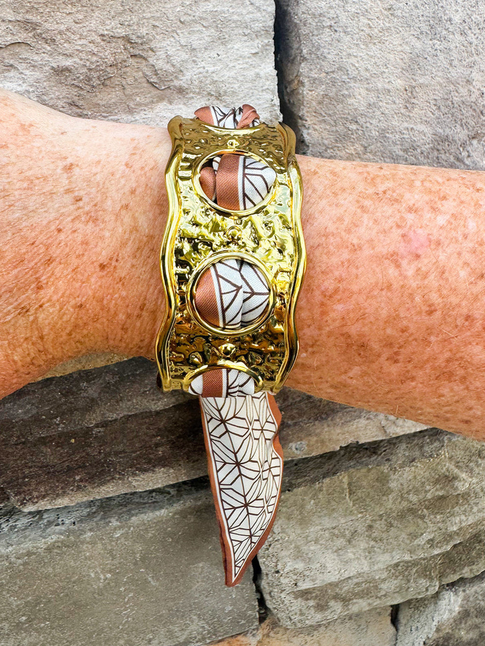 Gold cuff bracelet woven with geometric black-and-white scarf featuring a brown border; ties together for a bold yet feminine accessory.
