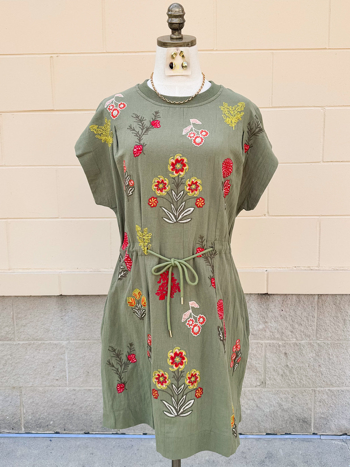 Sage green short sleeve mini dress with pink, yellow, and orange embroidered flowers and tie waist