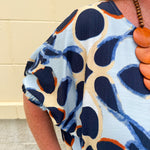 Printed short sleeve top in light blue with colorful indigo, orange, and yellow pattern, featuring a boat neck and relaxed A-line shape