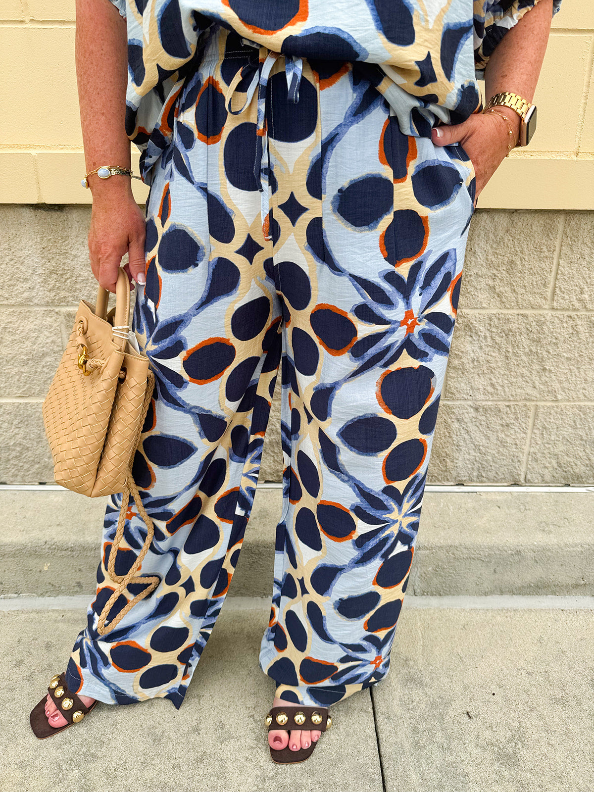 High-waisted printed pants in light blue with indigo, orange, and yellow pattern, featuring smocked waistband and straight leg fit