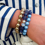 Layered charm bracelet stack featuring blue and gold glass beads, gold accents, and a tassel pendant for a stylish, boho-inspired look.