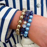 Layered charm bracelet stack featuring blue and gold glass beads, gold accents, and a tassel pendant for a stylish, boho-inspired look.
