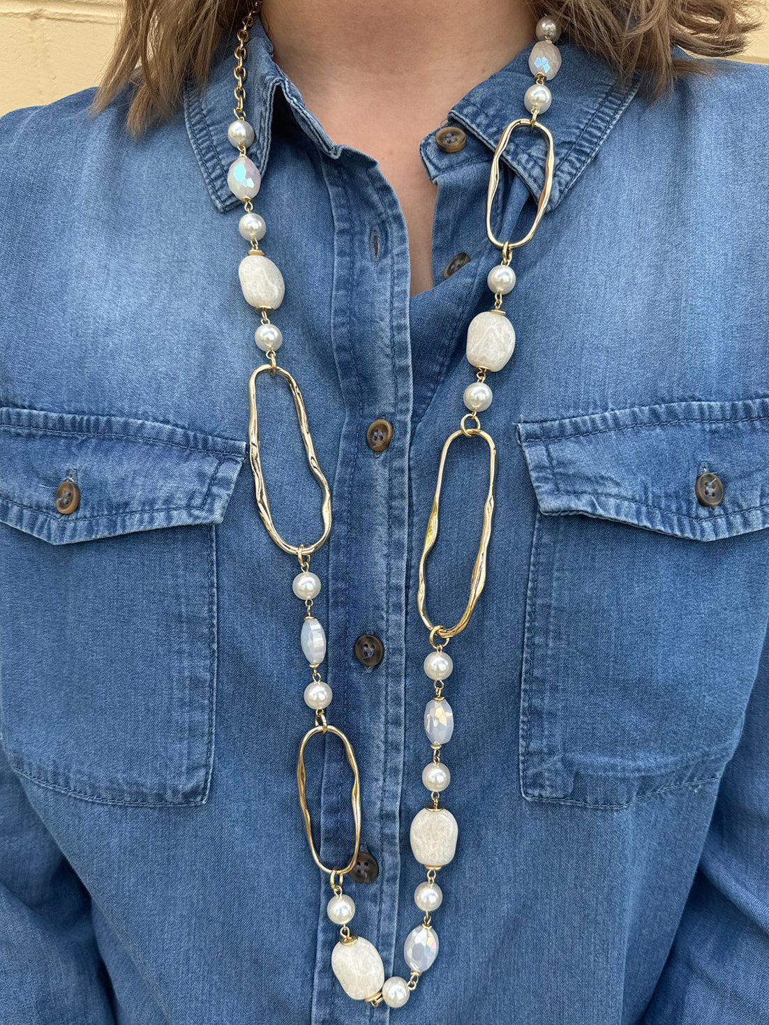 Long necklace with faux pearls and faceted stones draped on a display bust, showcasing layered textures