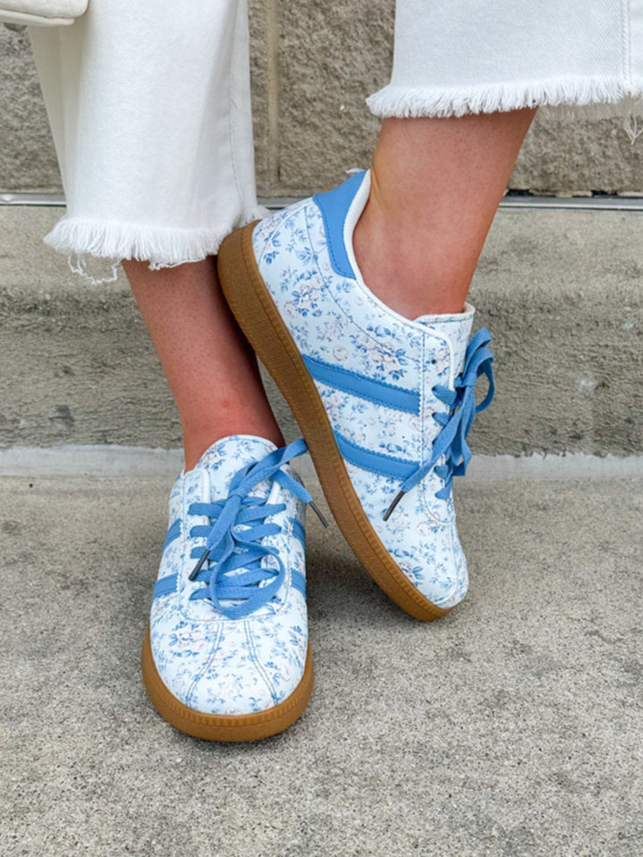 Blue floral sneakers with blue laces, side stripes, and tan rubber sole