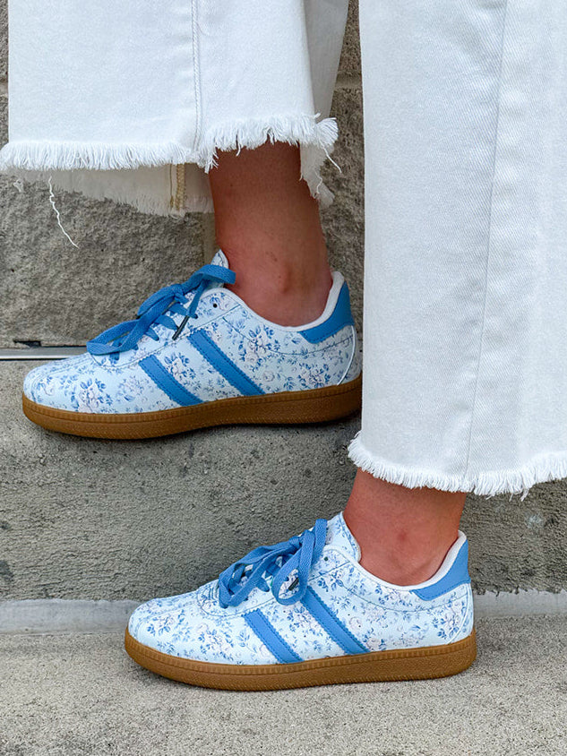 Blue floral sneakers with blue laces, side stripes, and tan rubber sole