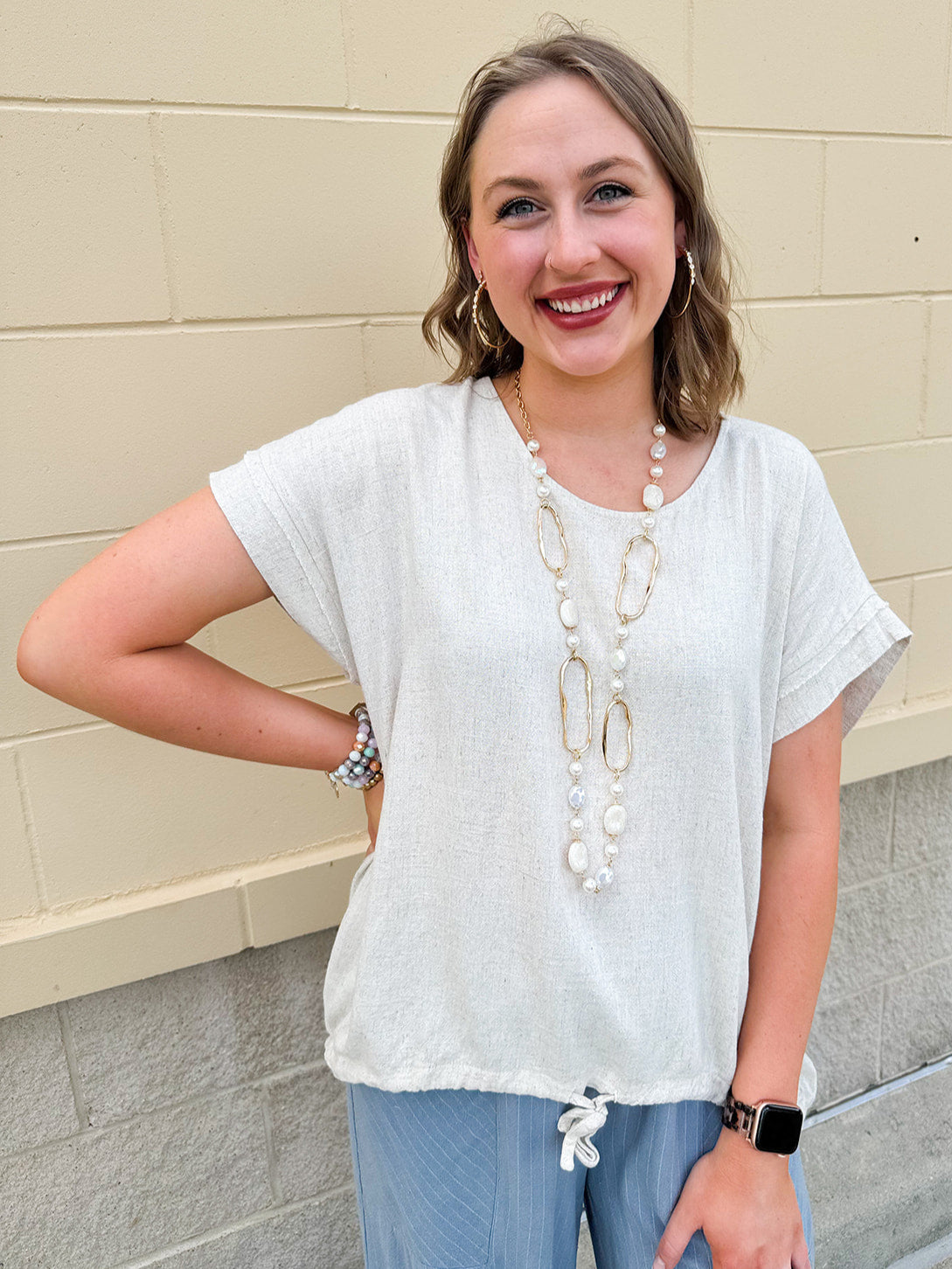 Linen-cotton blend short-sleeve top with front tie and raw hem in a soft neutral oatmeal shade.