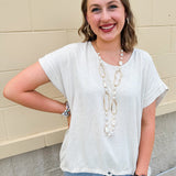 Linen-cotton blend short-sleeve top with front tie and raw hem in a soft neutral oatmeal shade.