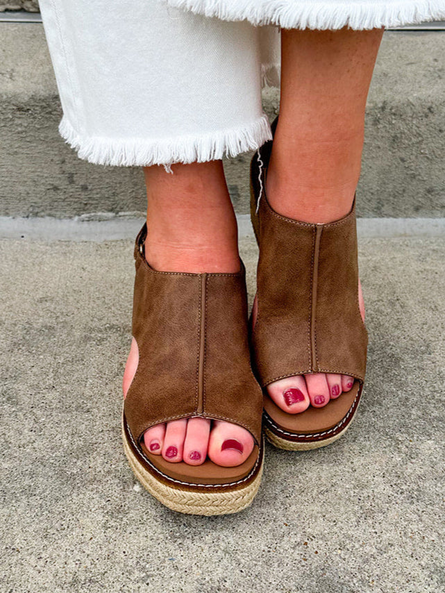 Chocolate brown vegan leather wedge with strap-back peep toe, open side slits, and raffia wedge bottom