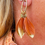 Caramel and gold-toned feather statement earrings displayed on a neutral background, highlighting texture and color