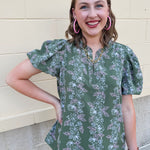 Green floral top with white and pink flowers, short sleeves, and V-neckline
