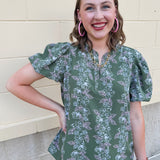 Green floral top with white and pink flowers, short sleeves, and V-neckline