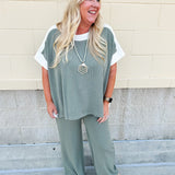 Sage green ribbed lounge pants with white waistband, drawstring, and large front patch pockets in a straight-leg fit