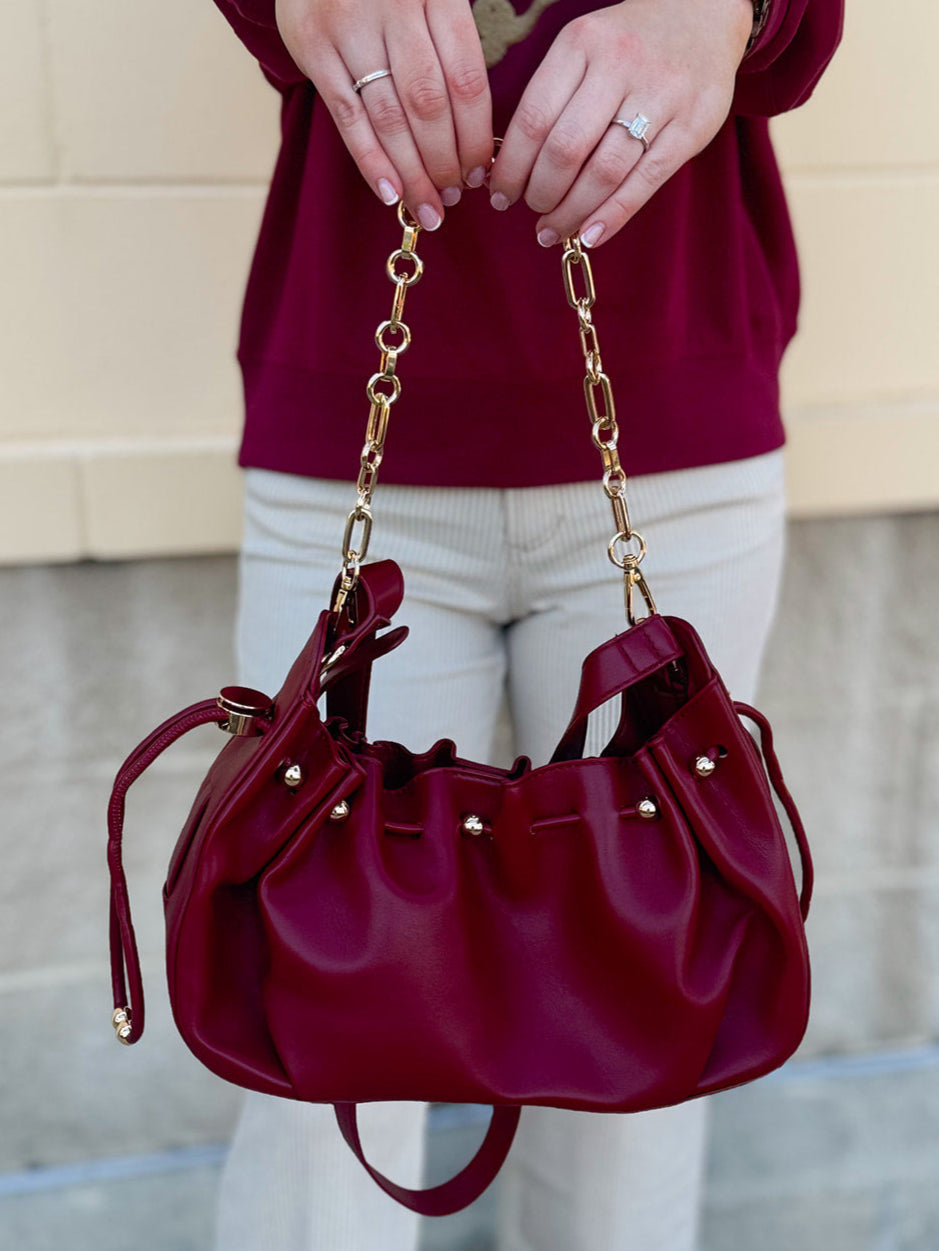 Deep garnet faux leather slouchy shoulder bag with gold chain straps and drawstring-style closure.