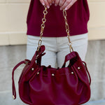 Deep garnet faux leather slouchy shoulder bag with gold chain straps and drawstring-style closure.