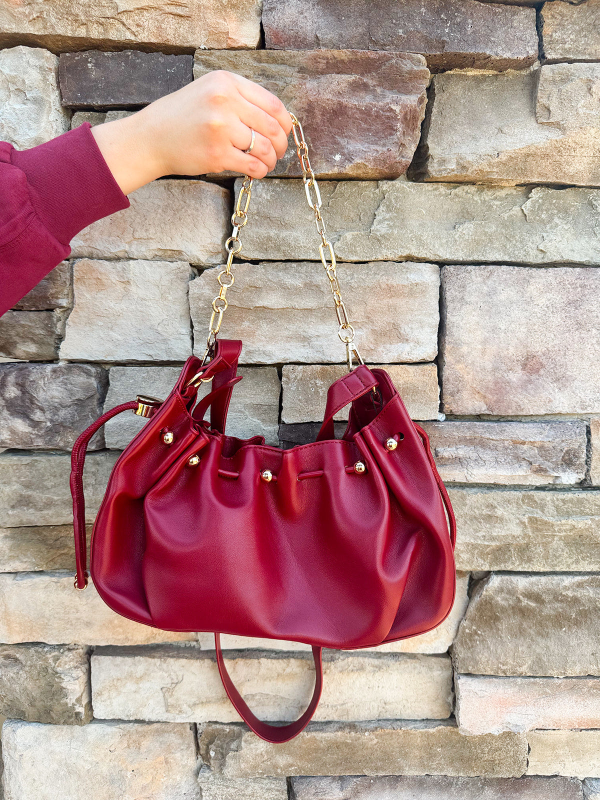 Deep garnet faux leather slouchy shoulder bag with gold chain straps and drawstring-style closure.
